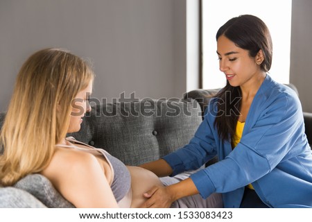 Expectant mother examined at home. Midwife touching belly of pregnant woman lying on couch. Midwifery concept