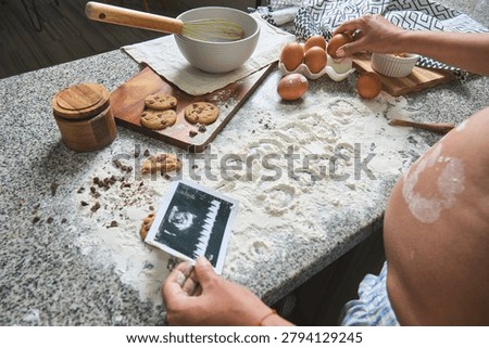 Expectant mother holding a sonogram while making cookies, symbolizing new life