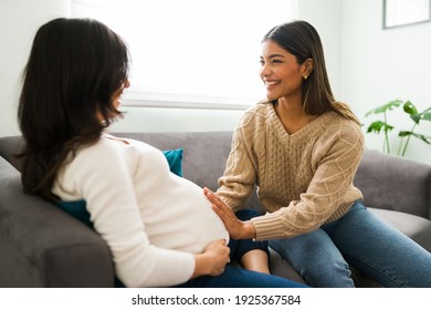 Expectant mother sitting on the sofa during a home visit from her happy doula. Smiling midwife touching the belly of a pregnant woman 