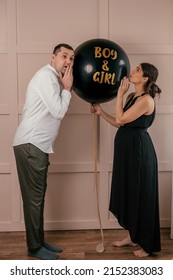 Expectant parents are having a gender reveal party.A married couple holds a black balloon with the inscription Boy and Girl.Family,pregnancy and prenatal care concept. - Shutterstock ID 2152383083