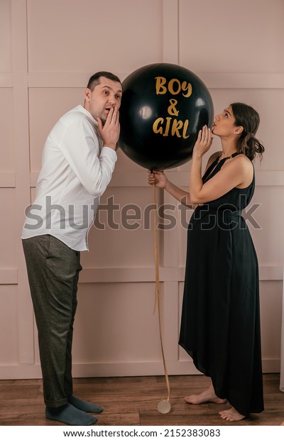 Expectant parents are having a\
gender reveal party.A married couple holds a black balloon with the\
inscription Boy and Girl.Family,pregnancy and prenatal care\
concept.