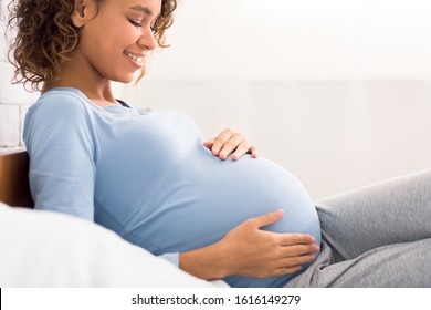 Expectation concept. Afro pregnant woman lying in bed and touching her belly