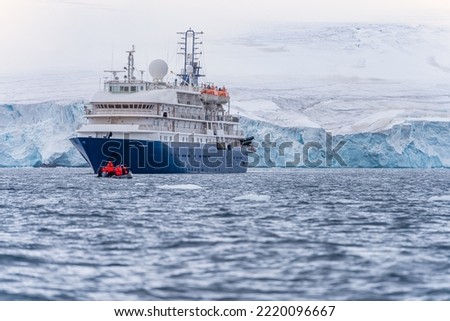 Expedition ship in front of Antarctic iceberg landscape in Cierva Cove - a deep inlet on the west side of the Antarctic Peninsula, surrounded by rugged mountains and dramatic glacier fronts.