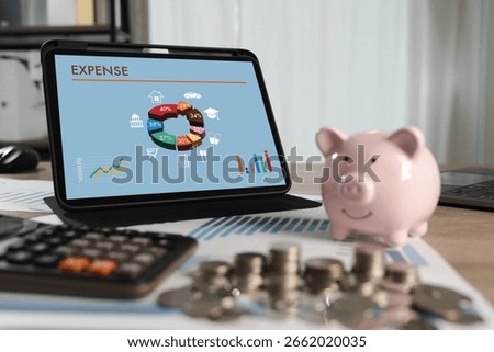 Expense analysis concept shown through colorful financial charts on a tablet screen as a person manages personal budgeting with coins, piggy bank, and calculator in a home office setup.