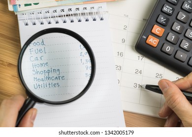 Expense and budget concept, hand holding magnifying glass over list of expense in small notepad and calculator on desktop calendar on wooden table. - Shutterstock ID 1342005179