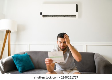 Expensive bills. Stressed latin man looking at the high electricity bill because of the air conditioning - Shutterstock ID 2149231727