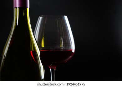 Expensive Bottle Of Wine And A Glass With Red Wine On A Dark Glossy Background.