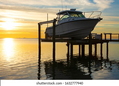 Expensive fishing boat on electric motorized dock vessel lift during sunrise with colorful sky.