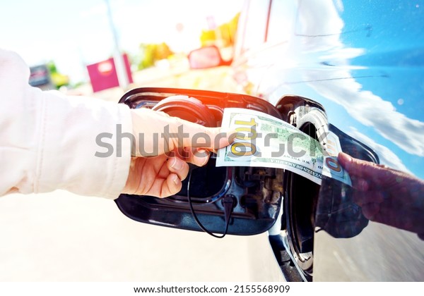 Expensive fuel\
concept. Rise in fuel price. Hand inserting a hundred dollar bill\
into the gas tank flap of a\
car.