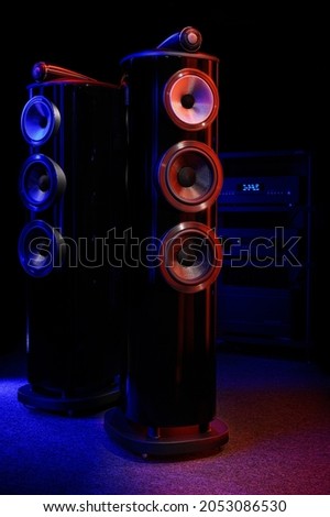 Expensive premium home floor acoustics in the dark. High-end amplifier, equipment rack, audiophile and music lover's room. Columns are isolated on a black background. Red and blue light.