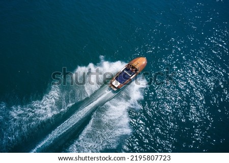 Expensive wooden classic italian boat with people moving faster on dark blue water top view. Fast moving expensive modern wooden boats aerial view.