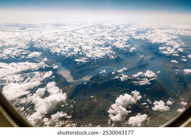 Experience the breathtaking aerial perspective of snow-covered mountains, vast lakes, and scattered clouds from a plane window. Perfect for travel, adventure, and nature enthusiasts. - Powered by Shutterstock