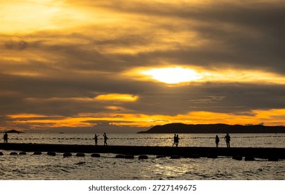 Experience a captivating sunset reflected on water with silhouettes of people strolling along a pier. The vibrant colors create a serene atmosphere.
