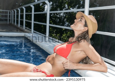 Experience the epitome of weekend bliss as a young woman indulges in leisure by the pool in this alluring photograph. The adult beauty, aged 25-29, exudes confidence and comfort.