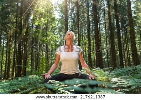 Experience the forest while bathing in the forest (Shinrin Yoku) with all senses. A 50 year old blonde woman sits cross legged relaxed. She fuels the sun and the atmosphere of the forest. Be h3althy. 