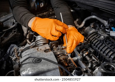 Experience the precision of a skilled mechanic's hands, clad in orange gloves, as they meticulously work to repair an open car engine in an auto service center, ensuring top-notch maintenance - Powered by Shutterstock