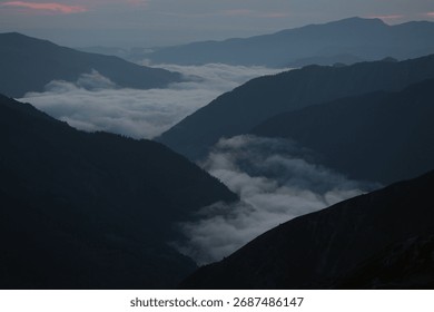 Experience profound tranquility as dawn breaks over majestic mountain ranges, with soft clouds revealing hidden valleys. Perfect for serene, inspiring projects.