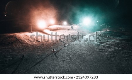 Experience the thrill of skiing under the stars with this stunning image of a night skiing run, lit with red and cyan lighting.