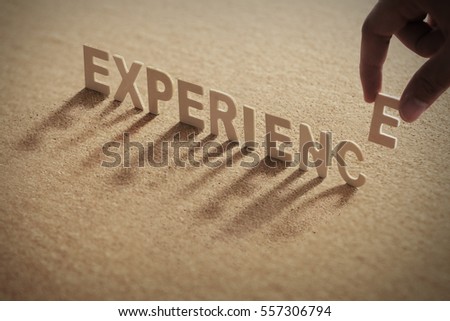 EXPERIENCE wood word on compressed or cork board with human's finger at E letter.