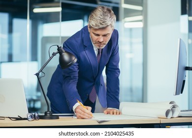 Experienced architect, working at the office desk on the drawing, makes final edits before handing over the object, a man in a modern office