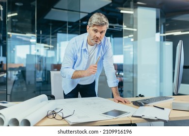 Experienced architect, working at the office desk on the drawing, makes final edits before handing over the object, a man in a modern office