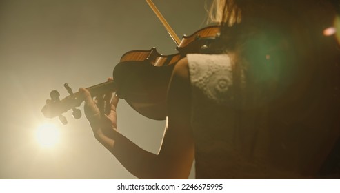 Experienced asian female violin player having a solo during the concert, spotted by light on black background 