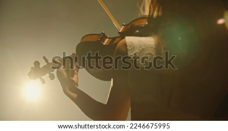 Experienced asian female violin player having a solo during the concert, spotted by light on black background 