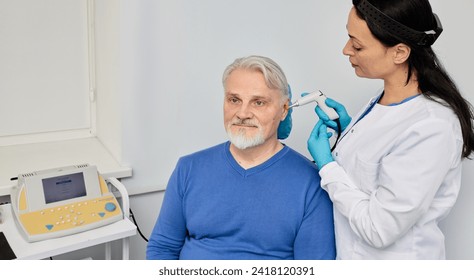 Experienced audiologist with tympanometer probe doing tympanometry procedure and impedance audiometry for senior male patient at audiology center - Powered by Shutterstock