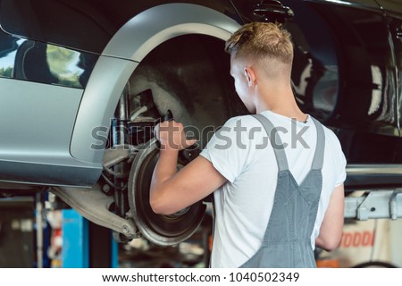 Experienced auto mechanic replacing the disk brakes of a lifted car during work in a modern automobile repair shop with professional tuning services