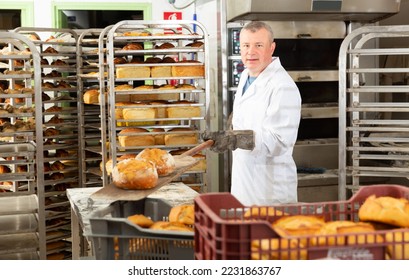 Experienced bakery worker pulling freshly baked loaves from industrial oven on wooden shovel .. - Powered by Shutterstock