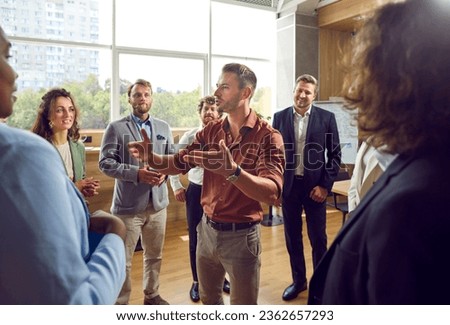 Experienced business coach meeting with a group of people. Young male business trainer or psychologist standing in a circle of men and women, talking about teamwork and giving professional advice