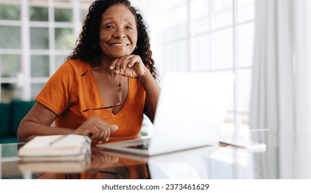 Experienced business woman working in her home office, with her laptop and a work journal on the table. Mature woman staying focused and productive, even in the comfort of her own home. - Powered by Shutterstock