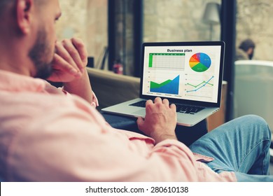 Experienced businessman looking at financial data with graphics and charts while work on a laptop computer, young entrepreneur analyzing performance on his notebook, male freelancer work in interior
