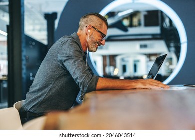 Experienced Businessman Smiling During A Virtual Meeting In A Modern Workplace. Mature Entrepreneur Using A Laptop For A Video Conference With His Partners. Businessman Sitting Alone In A Boardroom.