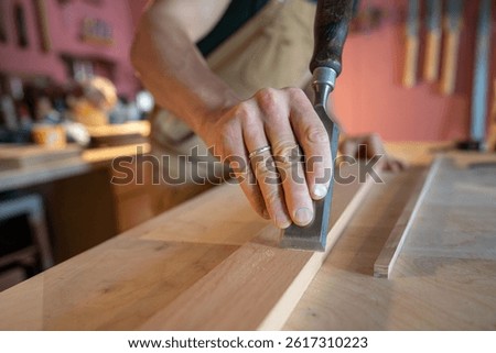 Experienced carpenter hands skillfully smoothing wood board surface with precise chisel removing imperfections. Detailed manual tool work, wood finishing sanding, surface refinement, craftsmanship