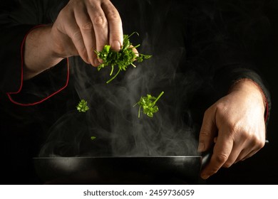 An experienced chef adds fresh parsley to a hot pan by hand. The concept of preparing a delicious breakfast with fresh herbs in a restaurant kitchen. - Powered by Shutterstock