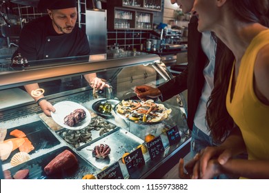 Experienced Chef Choosing Raw Seafood From The Freezer For Two Customers In A Trendy Restaurant Or Cafeteria With Fresh Food