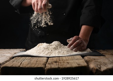 An experienced chef in a professional kitchen prepares the dough with flour to make Italian Italian pasta. concept of nature, Italy, food, diet and biology. on a dark background - Shutterstock ID 1928925617