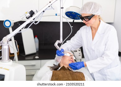 Experienced Concentrated Female Cosmetologist Performing Laser Facial Treatment To Elderly Woman In Aesthetic Medicine Office