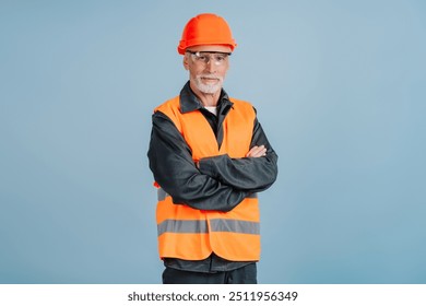 Experienced construction worker wearing a hard hat and safety vest is crossing his arms, conveying confidence and expertise on a blue background - Powered by Shutterstock