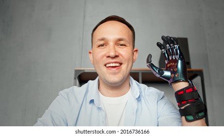 Experienced Disabled Company Worker Man Waves Artificial High Tech Hand Prothesis And Smiles At Video Conference Close View