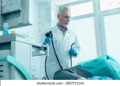 Experienced doctor holding a modern endoscope and looking at the patient lying on a medical couch