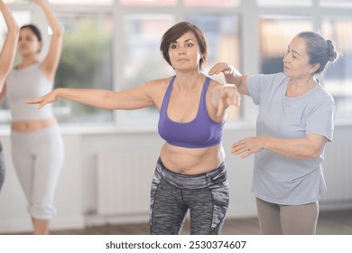 Experienced elderly female ballet instructor teaching middle aged woman beginner ballet positions in choreography studio during group class - Powered by Shutterstock