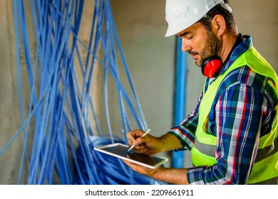 An Experienced Electrical Engineer Who Checks The Cables In The Building. He Uses A Tablet To Help With Work.