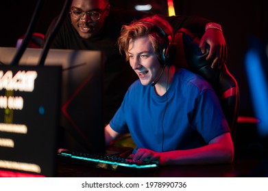 An experienced esports player shows his dark-skinned friend how to play an online video game in a computer club - Powered by Shutterstock