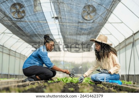 Experienced Farmer Mentoring a Young Apprentice on Plant Care Techniques in a Greenhouse.