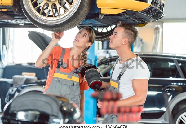 Experienced female auto mechanic checking\
tires before installing together with her colleague a new air\
suspension system in a modern automobile repair\
shop