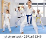 Experienced female karateka demonstrating kata sequence of movements to preteen daughter and son emphasizing hand striking techniques during family martial arts training ..