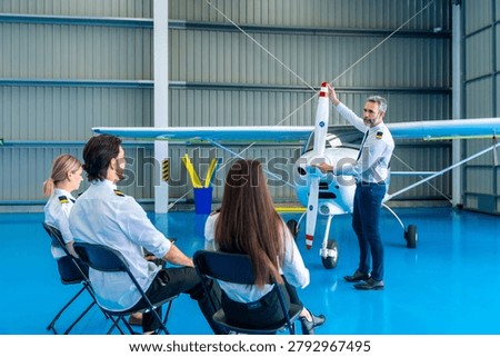 Experienced flight instructor giving a ground lesson about aircraft mechanics and operations to a group of aspiring pilot students in a training facility hangar