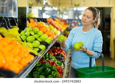 experienced hostess came to supermarket of vegetables and fruits. She chooses juicy apples in window - Powered by Shutterstock